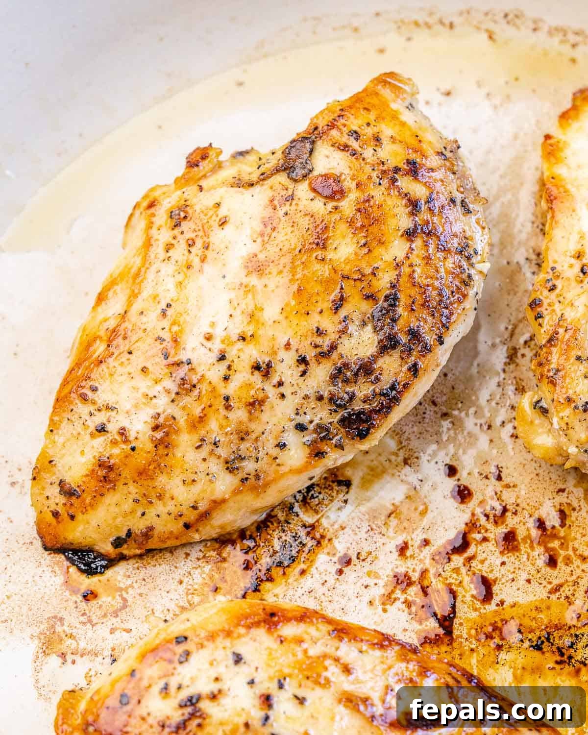 Close-up of golden-brown seared chicken breast resting in a skillet, showcasing its perfectly cooked exterior.