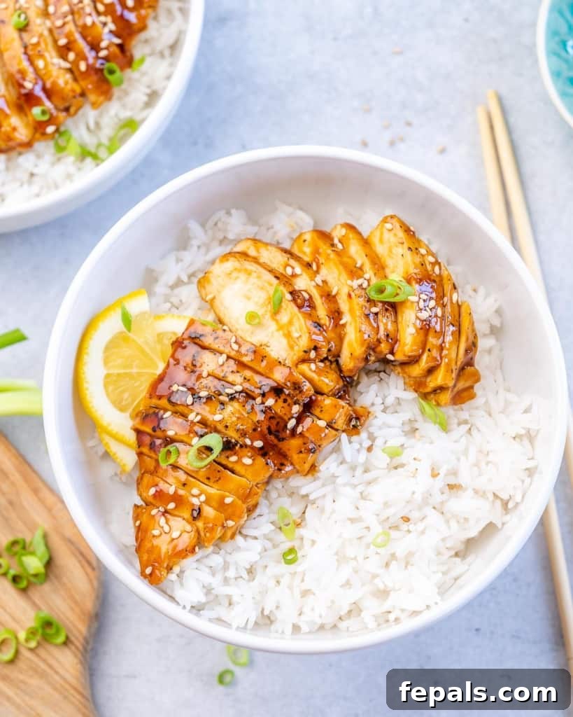 Top view of an elegant white bowl filled with teriyaki chicken, garnished with green onions, resting on a rustic wooden surface.