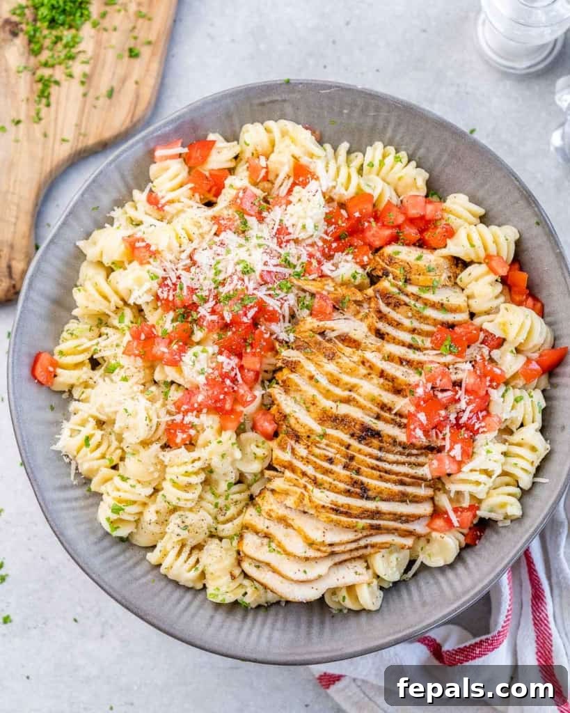 An overhead shot of a gray ceramic bowl filled with creamy Cajun chicken pasta, generously garnished with freshly chopped red tomatoes, enhancing its visual appeal and adding a burst of freshness.