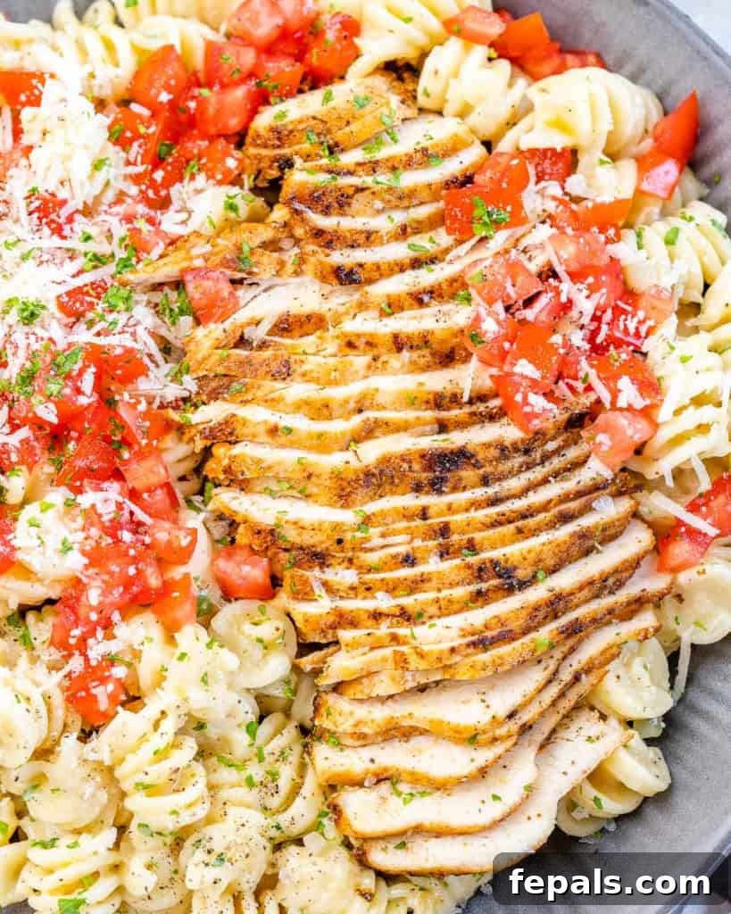 A close-up shot of tender, sliced Cajun chicken breast generously placed over a bed of creamy, al dente pasta, highlighting the rich textures and vibrant flavors.