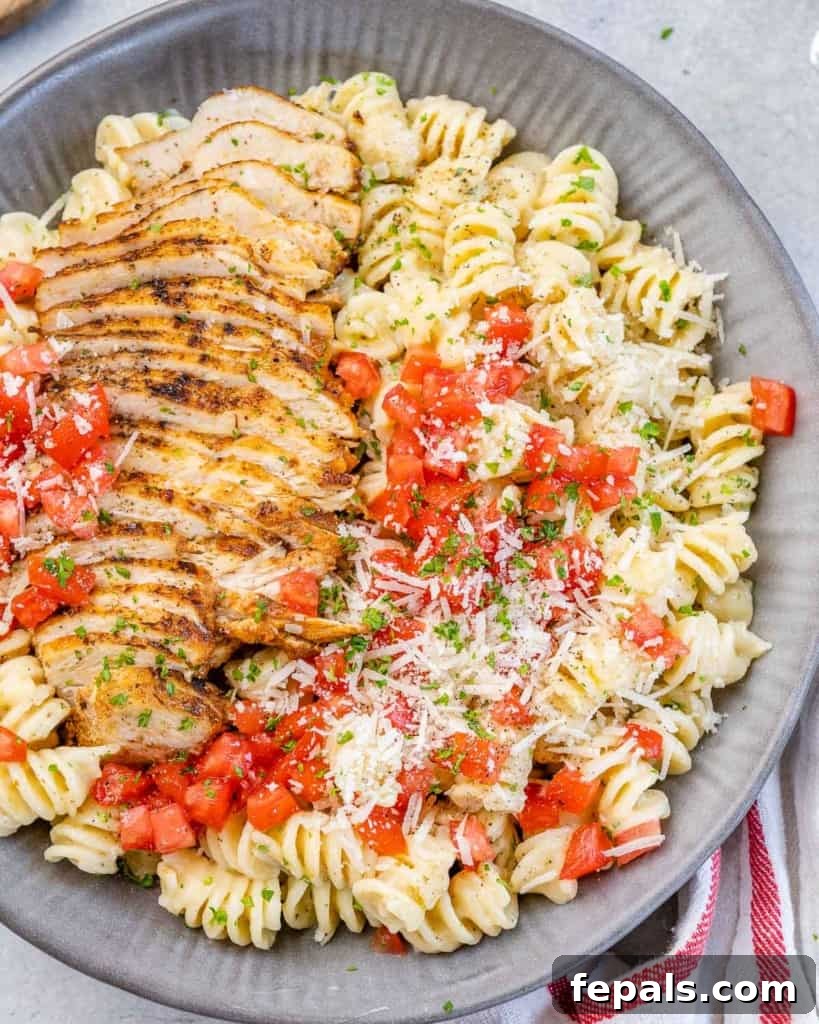 An inviting top-down view of creamy chicken pasta presented in a stylish gray bowl, meticulously garnished with fresh tomatoes, ready to be savored.
