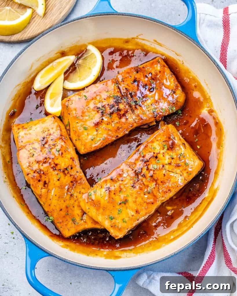 Top view of salmon in a pan garnished with fresh lemon wedges.