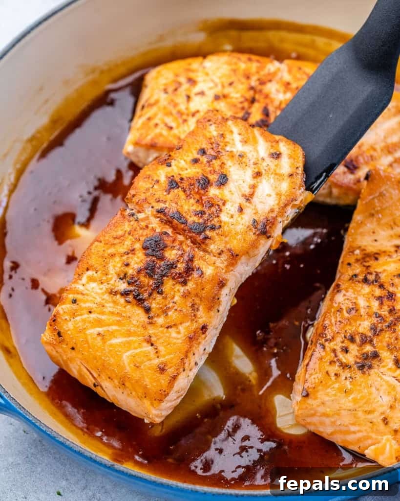 A salmon fillet being returned to the pan, coated in the rich honey garlic sauce.