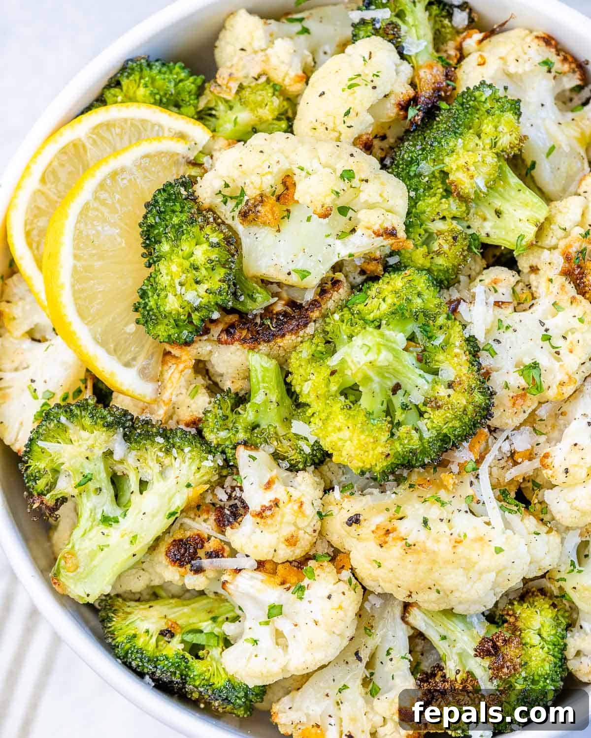close view of roasted cauliflower and garlic with lemon wedges, beautifully browned