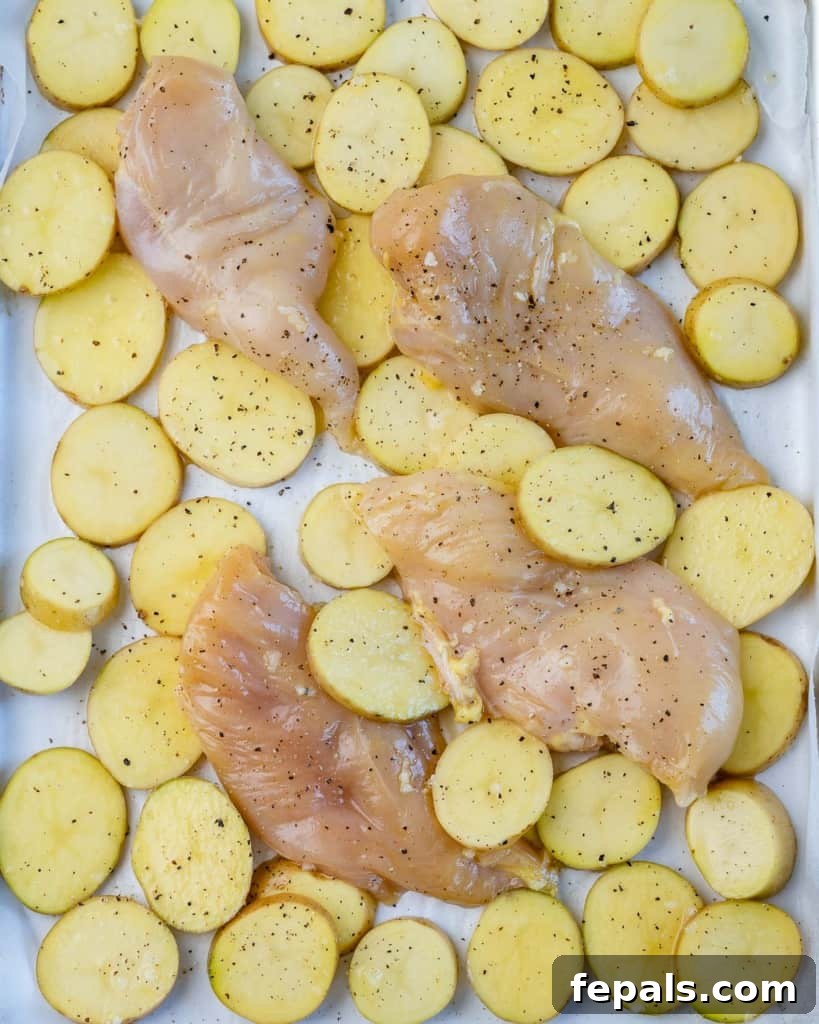 raw chicken breast and sliced baby potatoes arranged on a parchment-lined sheet pan, coated in marinade, before baking