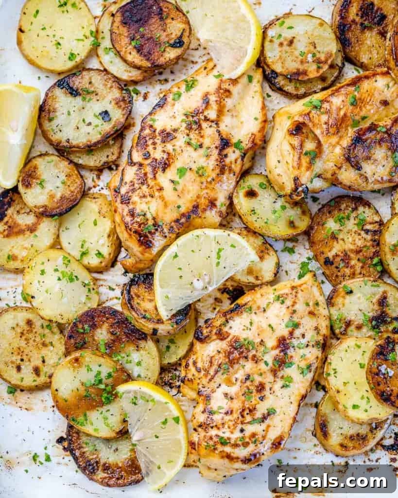 close up shot of a baked lemon chicken breast with golden brown crust, served with tender roasted potatoes on a sheet pan
