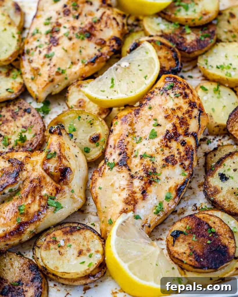 close up top view of baked honey lemon chicken breast on a sheet pan with roasted potatoes and fresh lemon wedges, ready to serve