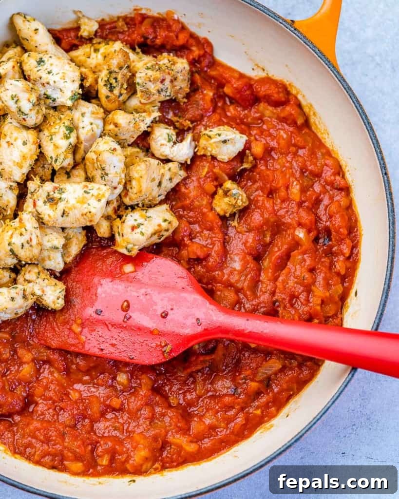 Comforting Chicken Parmesan Pasta 5 chicken bites over marinara sauce in a pan with a red spatula in it