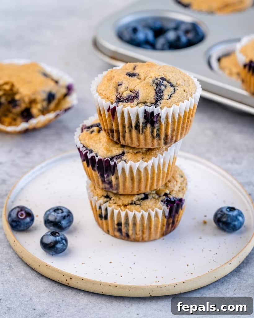 Side shot of three perfectly baked, healthy blueberry muffins stacked on a white plate.