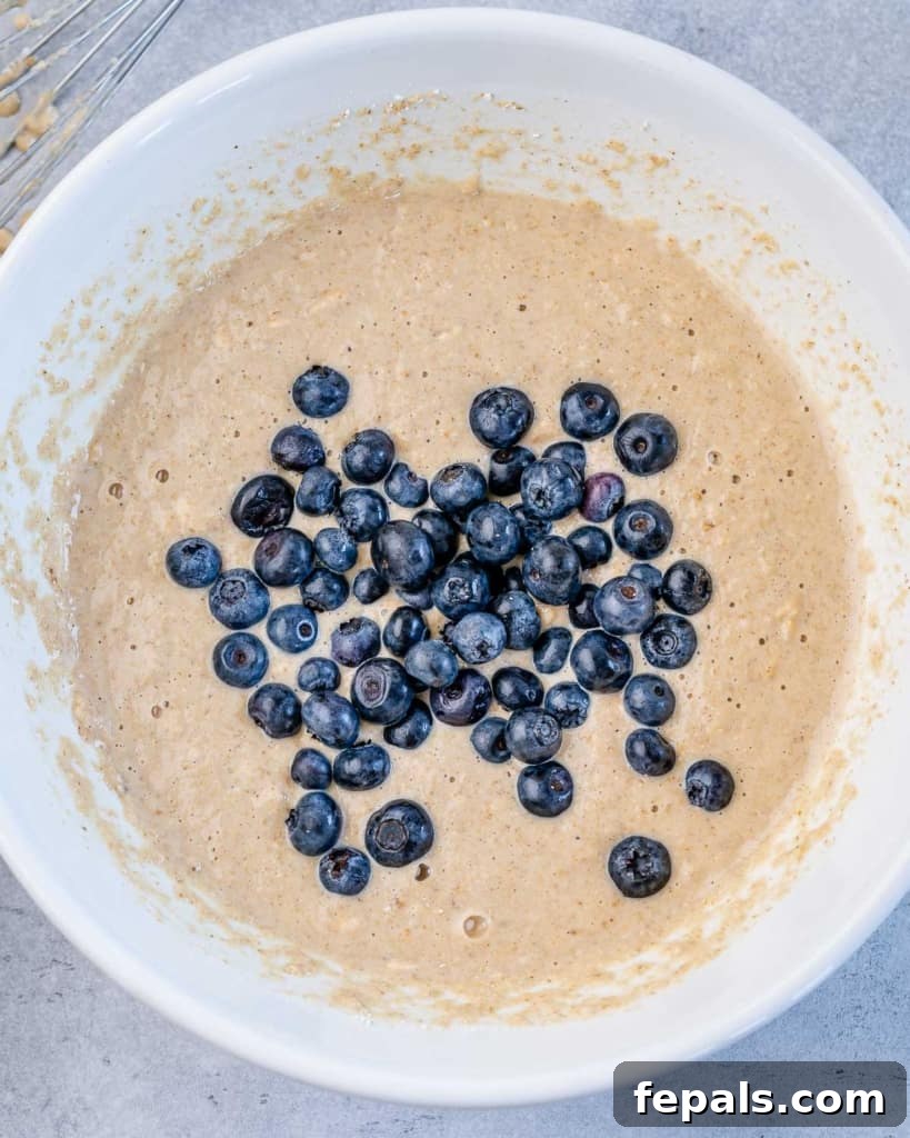 Fresh blueberries being gently folded into the muffin batter in a mixing bowl.