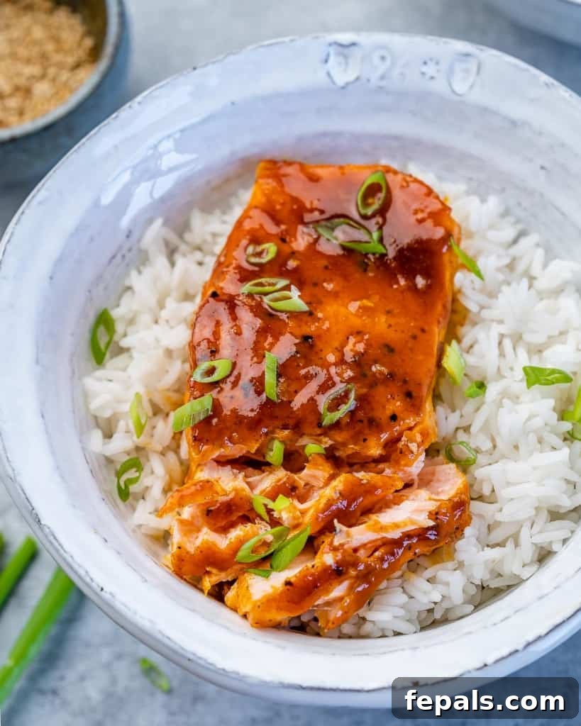 Sweet and Sticky Pan Seared Salmon 2 flaked baked honey salmon over white rice in a white bowl garnished with sliced green onions