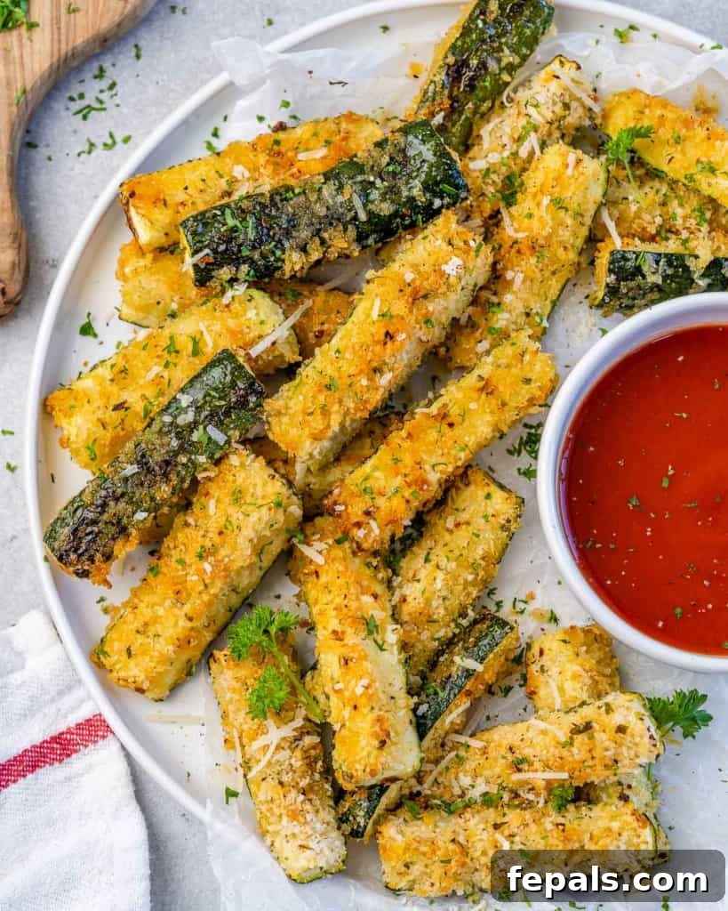 Crispy Air Fryer Zucchini Parmesan Fries 9 close up zucchini fries with a side of red dipping sauce on a white plate