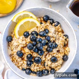 Berry Bliss Overnight Oats 13 top view of overnight oatmeal in a white bowl topped with blueberries and maple syrup with 2 lemon slices to garnish