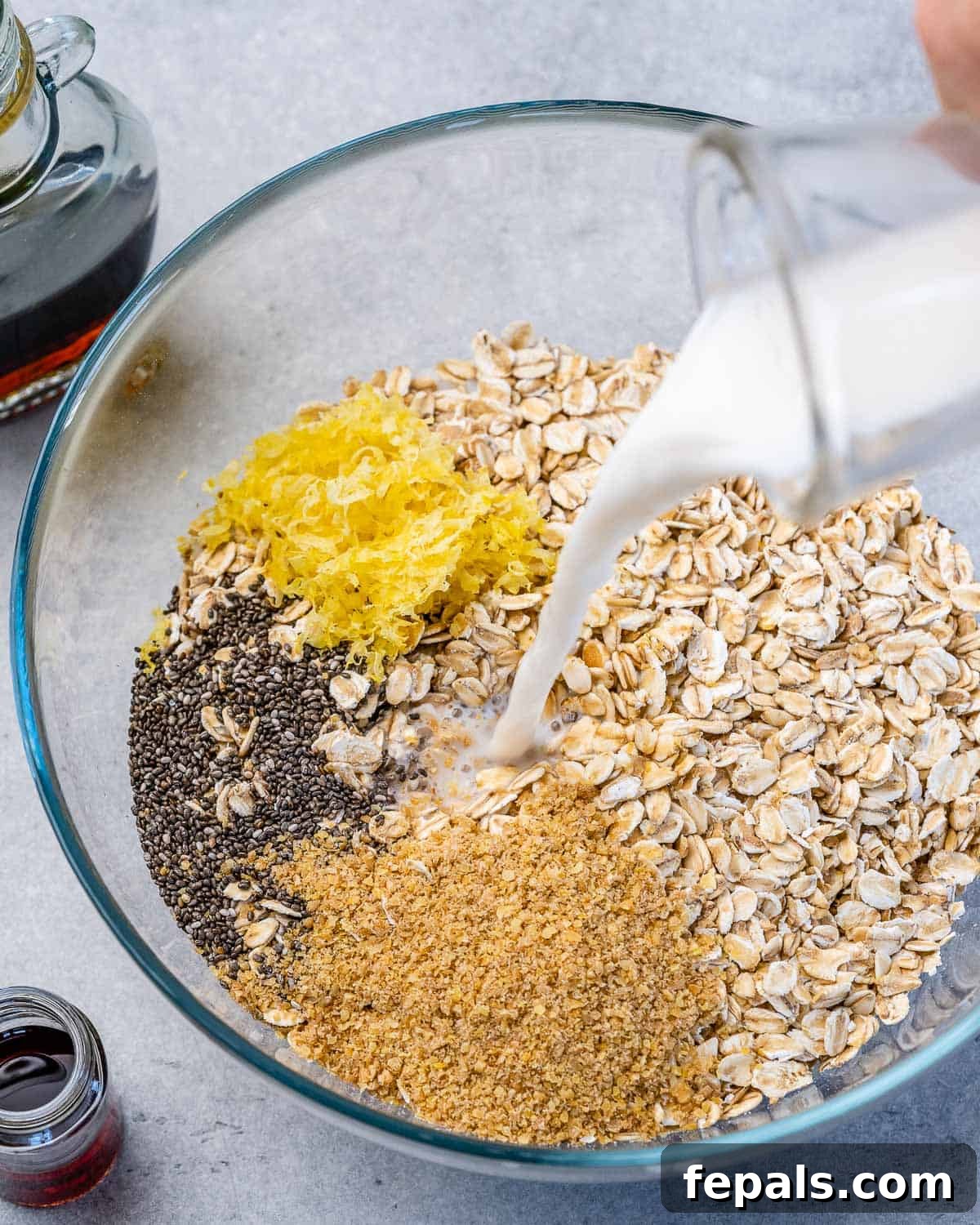 Berry Bliss Overnight Oats 7 A bowl with oats, lemon zest, chia seeds, flax seeds, and milk being mixed together before blueberries are added.