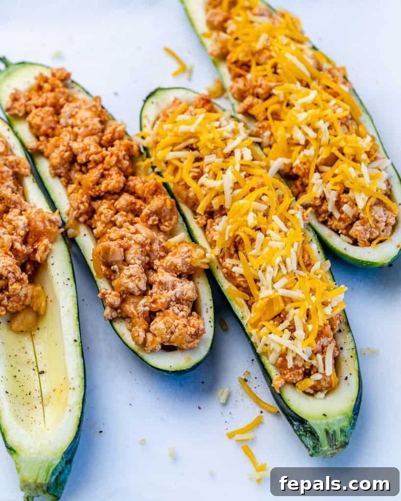 Fiery Buffalo Chicken Zucchini Boats 7 Buffalo chicken stuffing being carefully spooned into the zucchini boats, which are then topped with a generous layer of shredded cheese, ready for baking.