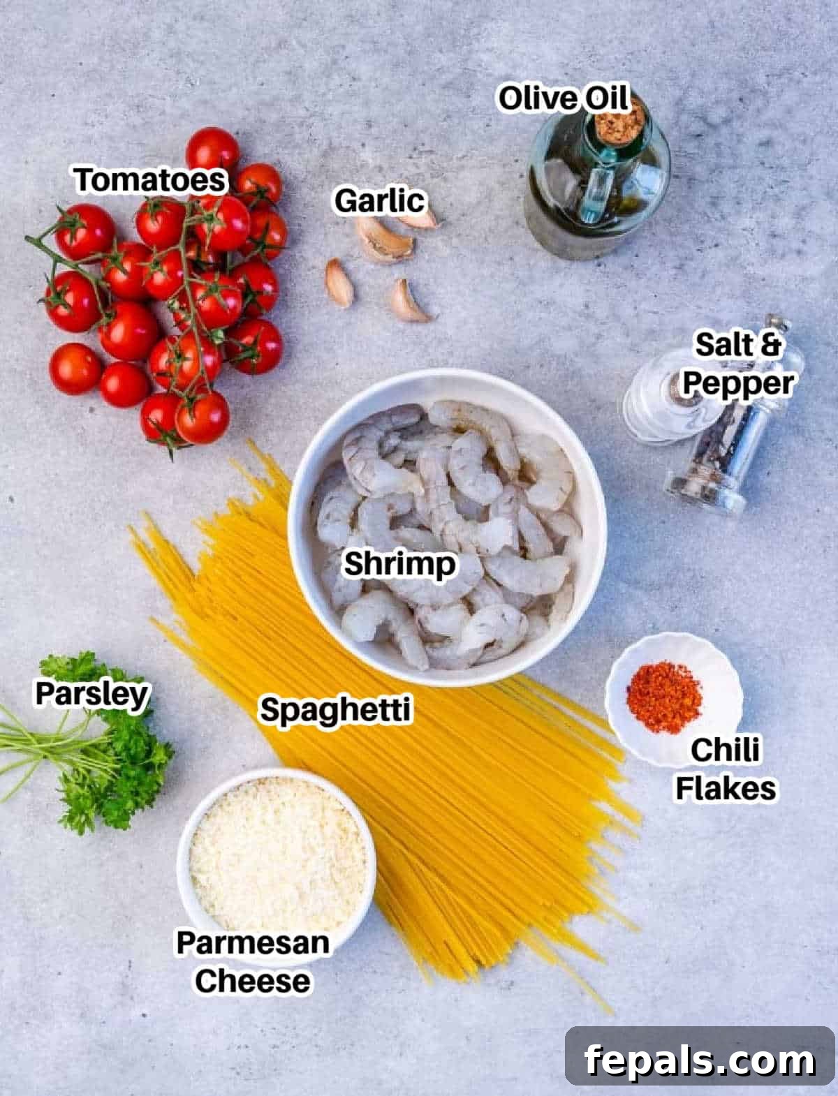 A flat lay image displaying all the fresh ingredients needed to make garlic shrimp pasta, including spaghetti, olive oil, garlic, raw shrimp, chili flakes, cherry tomatoes, Parmesan cheese, and parsley.