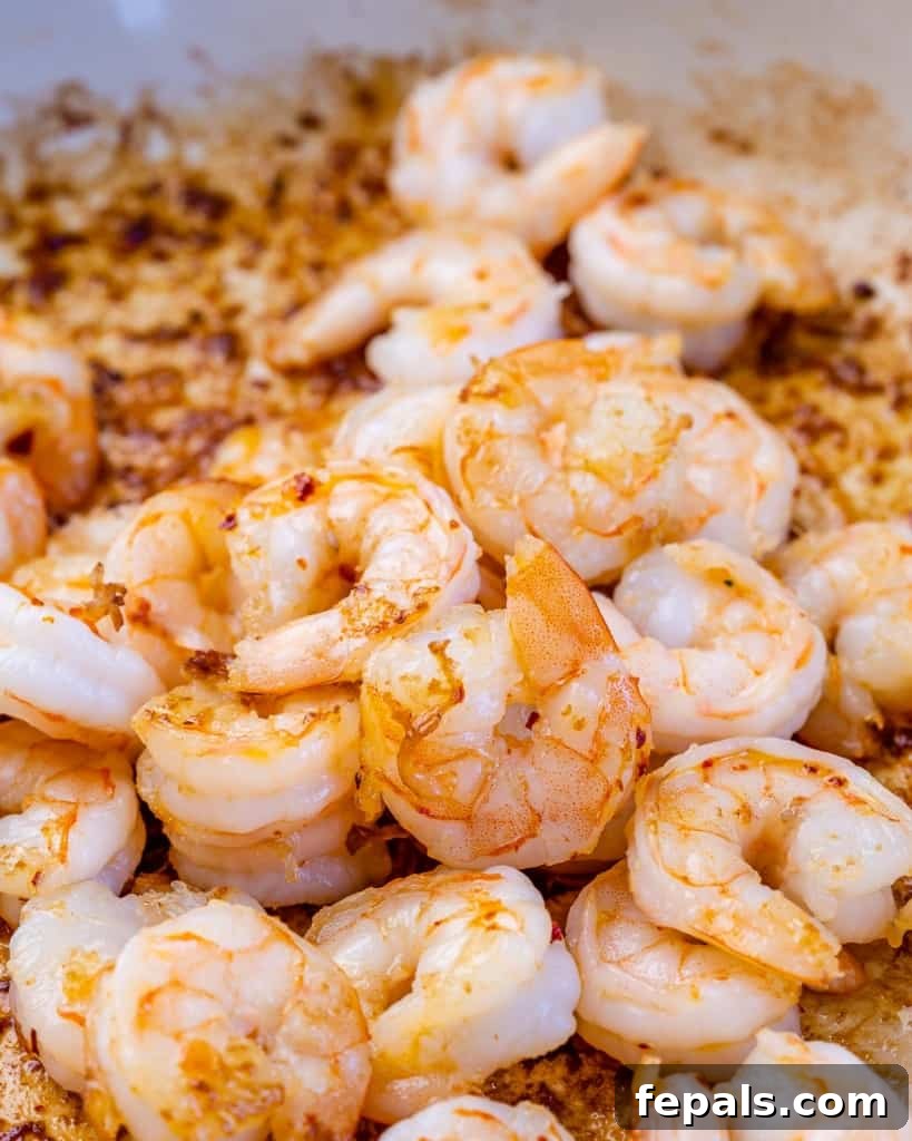 Close-up view of raw shrimp sizzling in a pan with garlic and olive oil, turning pink as it cooks.