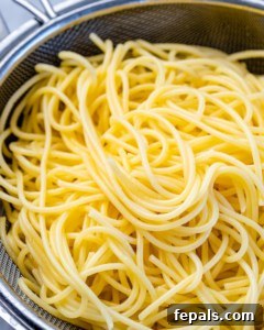 Cooked spaghetti noodles draining in a colander.