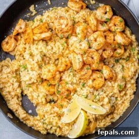 top view risotto in black skillet topped with shrimp in a black skillet with 3 lemon wedges to garnish