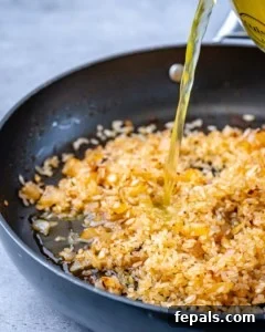 broth being poured over seasoned rice in a skillet to make risotto