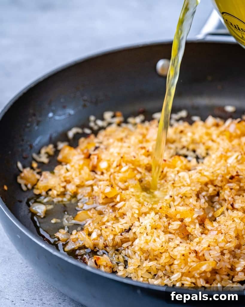 Golden Garlic Shrimp Risotto 6 broth being poured over seasoned rice in a skillet to make risotto