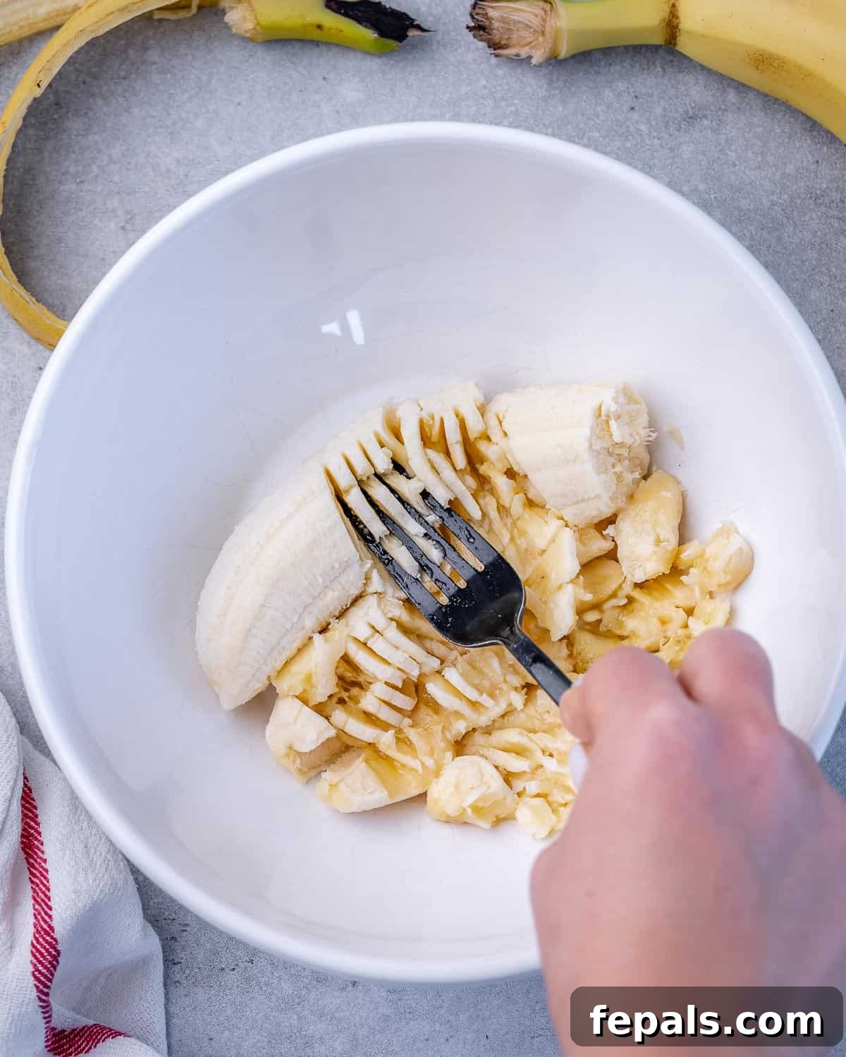 Mashing Bananas for Healthy Oatmeal Bars A close-up shot of ripe bananas being mashed smoothly with a fork in a round white bowl, preparing them for the oatmeal bar mixture.