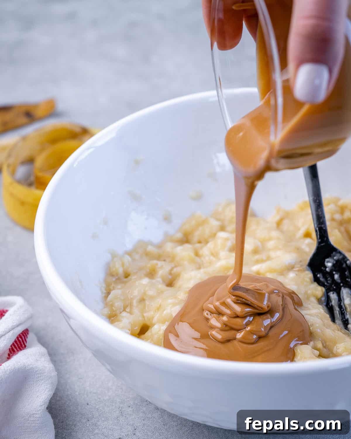 Wholesome Oat Energy Bars 3 A jar of natural peanut butter being poured into a bowl containing mashed bananas, illustrating the first step of combining wet ingredients.