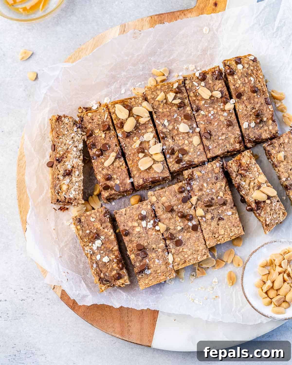 Wholesome Peanut Butter Banana Oatmeal Bars Twelve neatly cut squares of healthy oatmeal bars, generously topped with peanuts and chocolate chips, arranged on parchment paper.