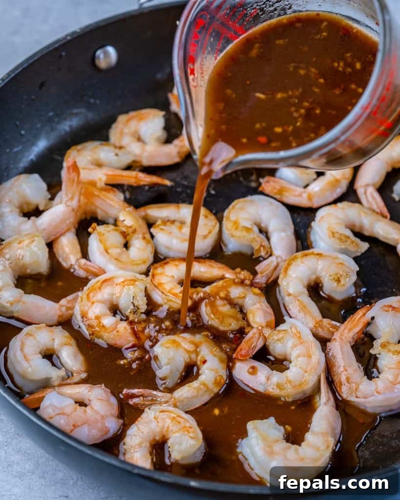 teriyaki sauce being poured over shrimp in a black skillet