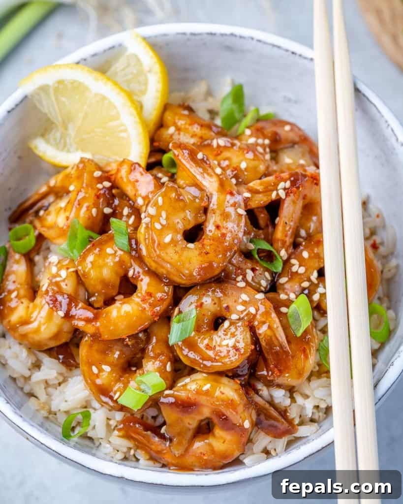 top view of teriyaki shrimp over rice in a white bowl with two side of chop sticks 