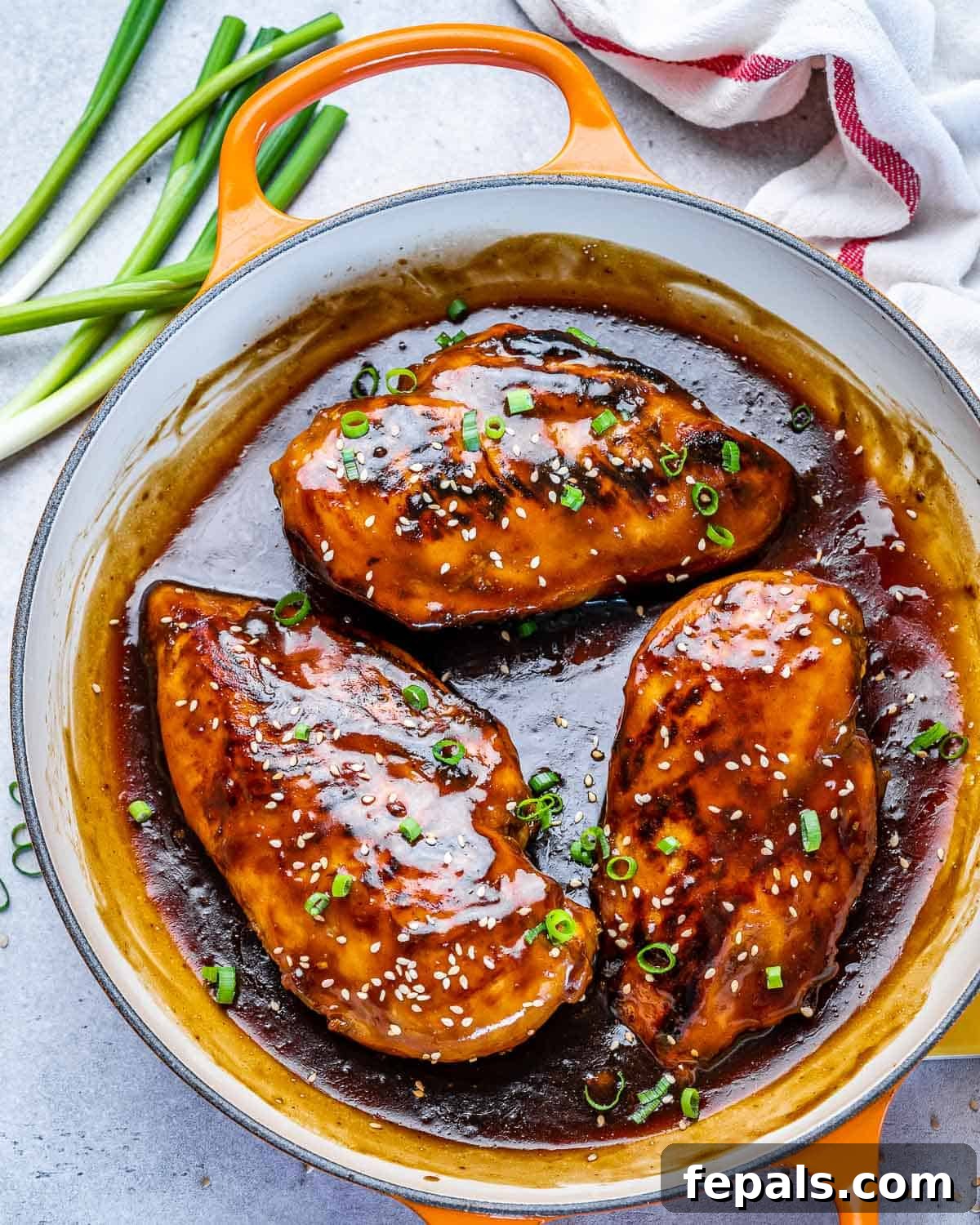 top view of four chicken breasts in sauce with green onions and sesame seeds