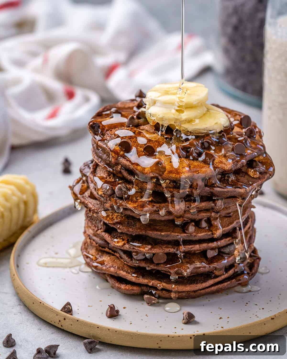 Easy Chocolate Banana Pancakes A tall stack of healthy chocolate oatmeal pancakes topped with fresh banana slices, chocolate chips, and a drizzle of maple syrup, ready for a delicious breakfast.
