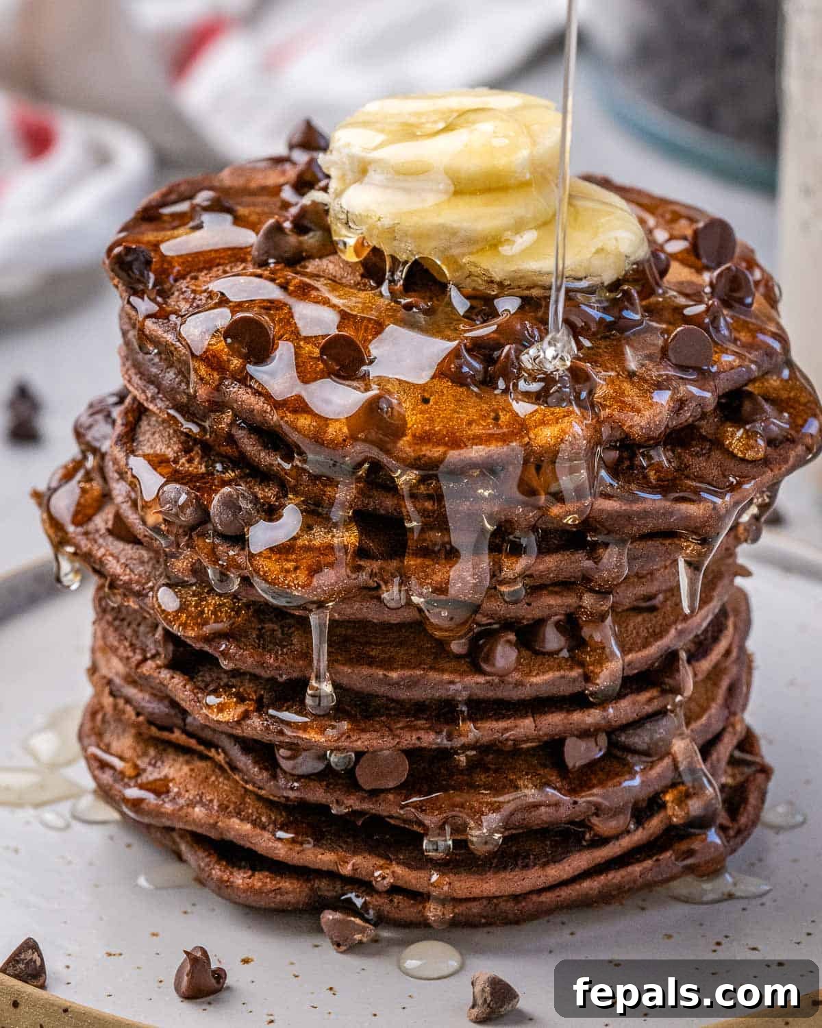 A delicious stack of chocolate oat pancakes topped with a swirl of syrup and fresh banana slices, served on a rustic plate.