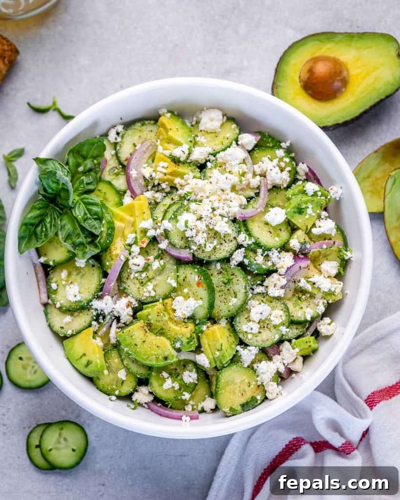 top view of cucumber feta salad in a white bowl and a side of half fresh avocado