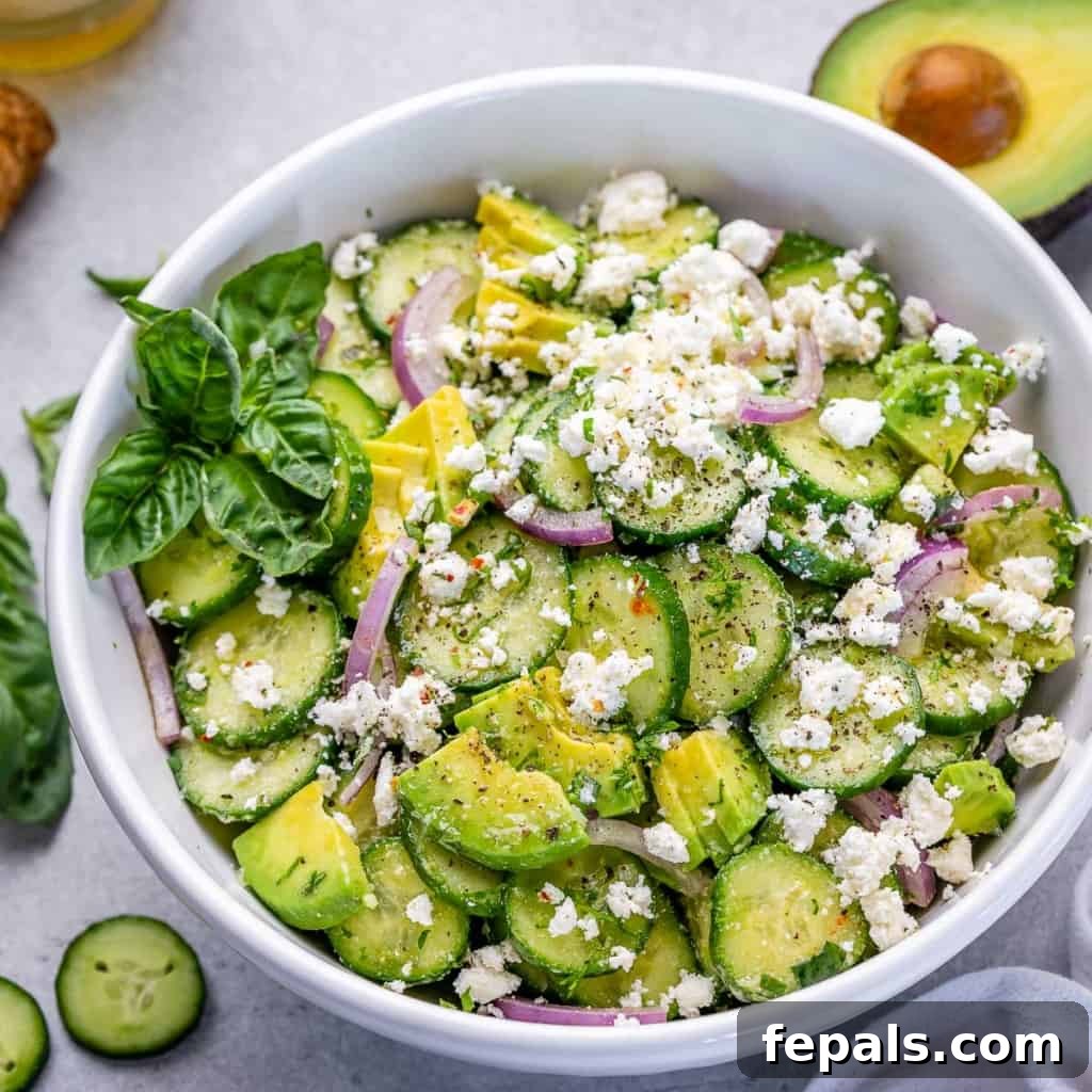 side shot of cucumber salad in a white bowl, topped with feta cheese and fresh basil garnish on the left side of the bowl