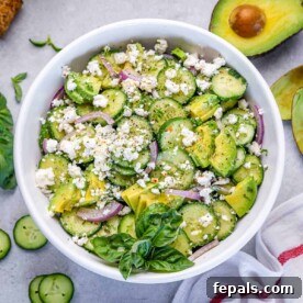 a white round bowl with cucumber avocado and feta salad with basil garnish.