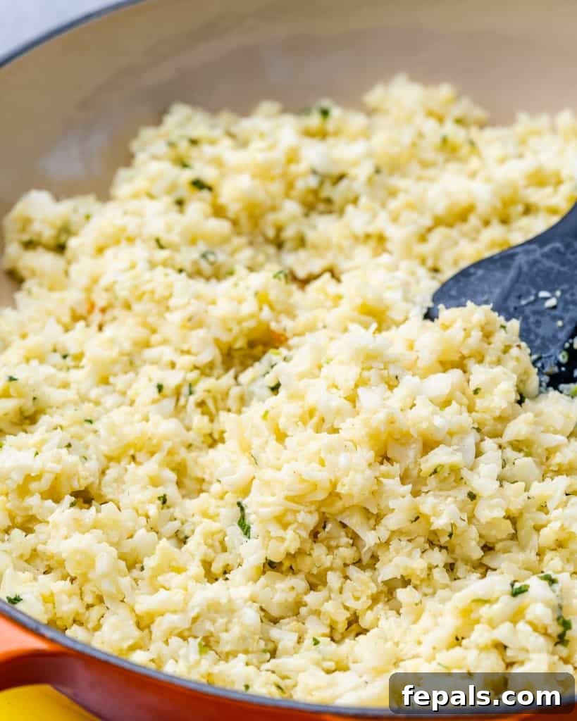 Golden Pan-Seared Lemon Garlic Chicken 6 Cauliflower rice being cooked in an orange skillet, absorbing the flavorful lemon garlic sauce.