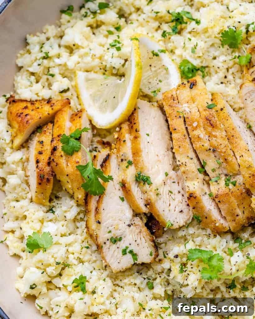 Golden Pan-Seared Lemon Garlic Chicken 9 Close up view of the finished lemon garlic chicken breast over cauliflower rice in an orange skillet, garnished with fresh cilantro and lemon slices.