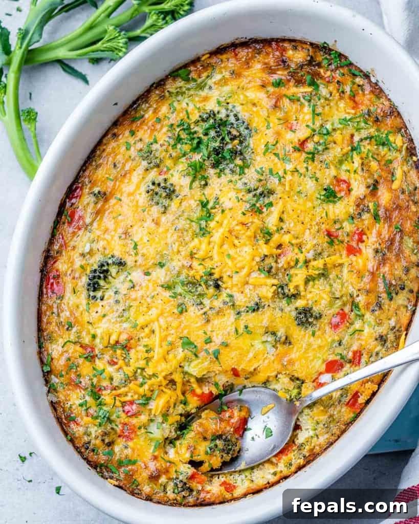 Savory Broccoli Cheddar Breakfast Bake 2 top view breakfast casserole with veggies, cheese, in a white dish with spoon in it