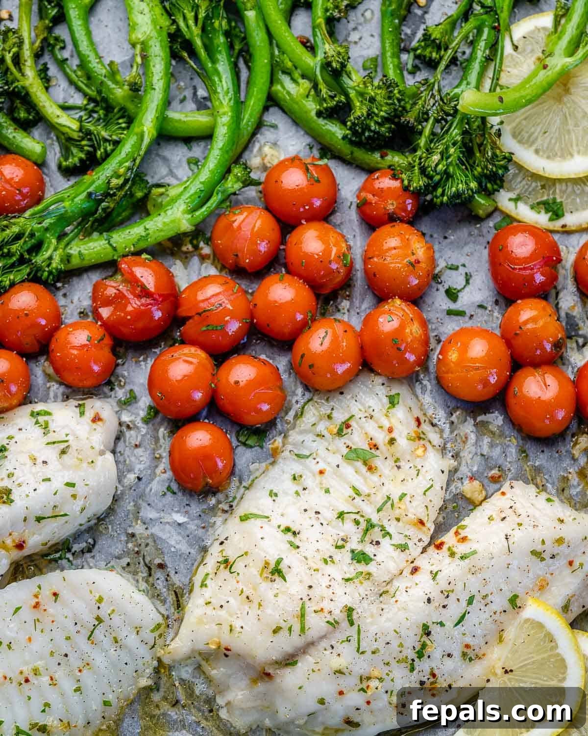 Easy Baked Tilapia top view of baked tilapia on sheet pan with tomatoes and broccolini with lemon wedges