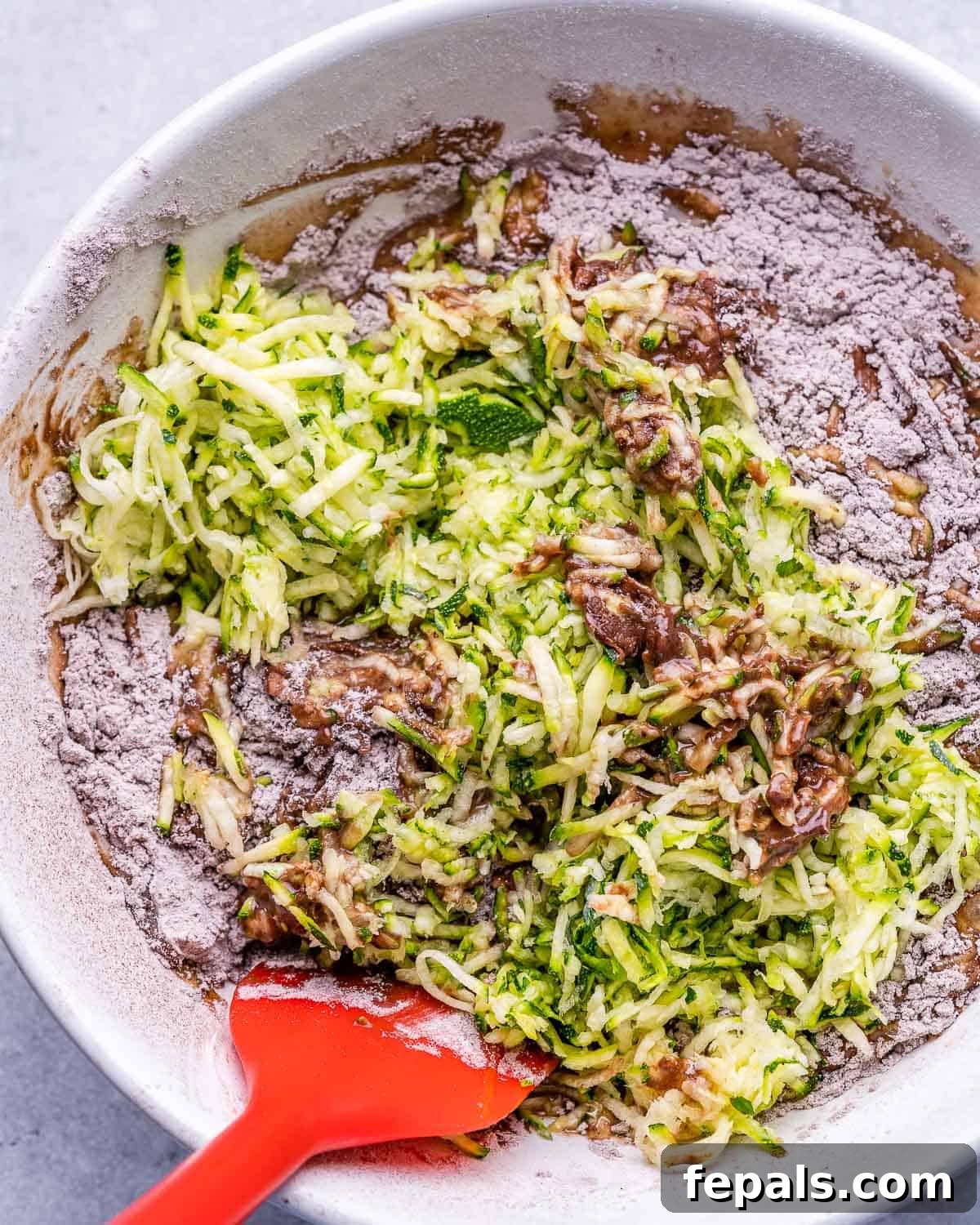 zucchini bread batter being mixed with red spatula
