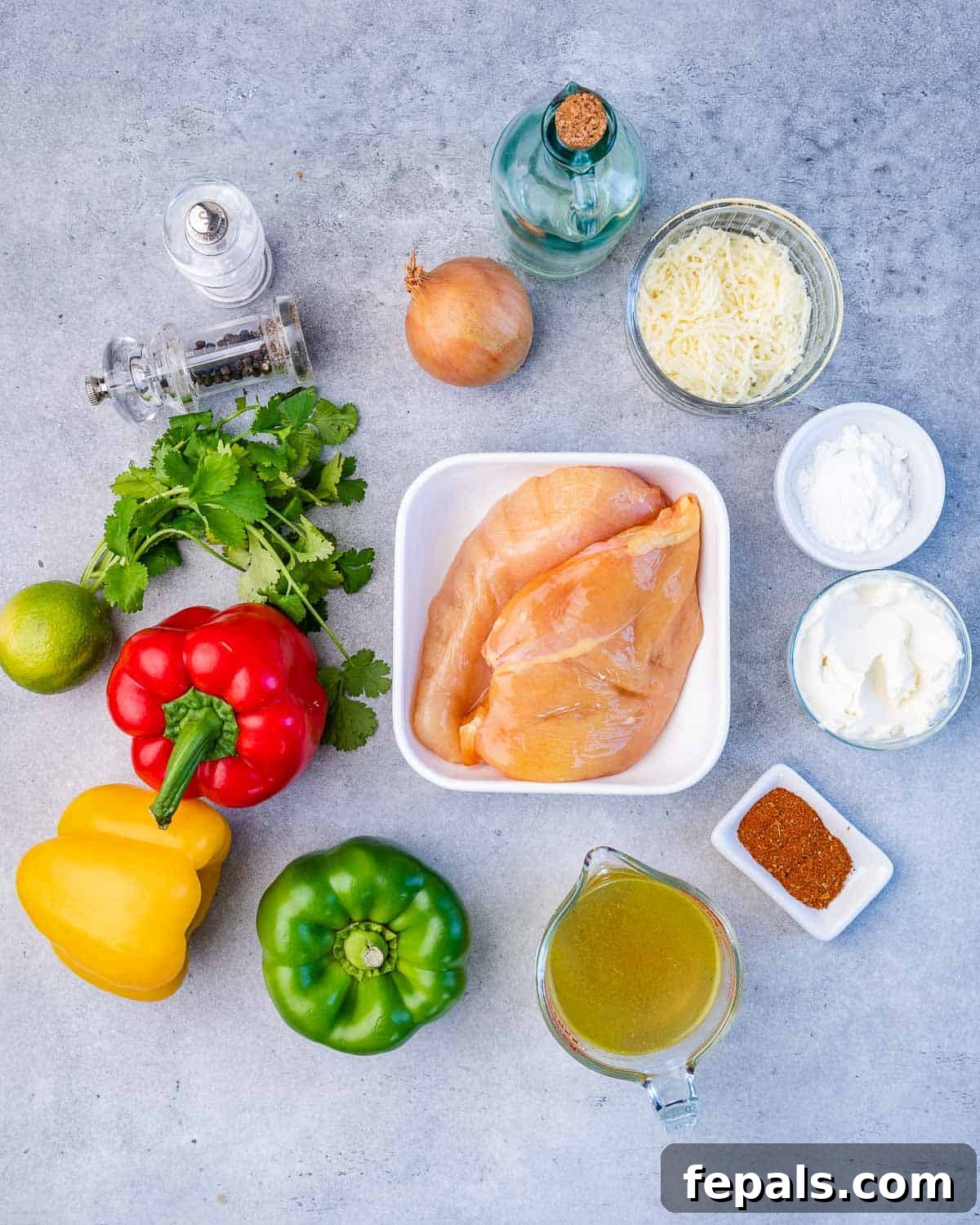 Dreamy Creamy Chicken Fajita Skillet 5 A flat lay of all fresh ingredients for creamy chicken fajitas: cilantro, colorful bell peppers, shredded mozzarella, chicken breasts, cornstarch, fajita seasoning, avocado oil, lime, salt, pepper, and onion.