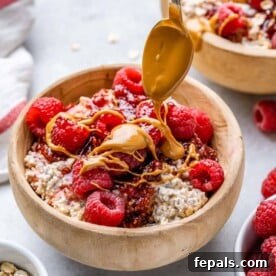 overnight oats in a brown wooden bowl topped with peanut butter drizzle and raspberries, ready for a healthy breakfast.