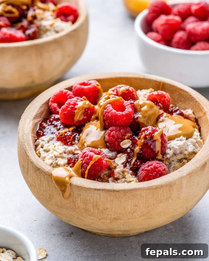 Dreamy PB&J Overnight Oats 3 side shot of creamy peanut butter and jelly overnight oatmeal in a tan wood bowl topped with fresh berries and rich peanut butter