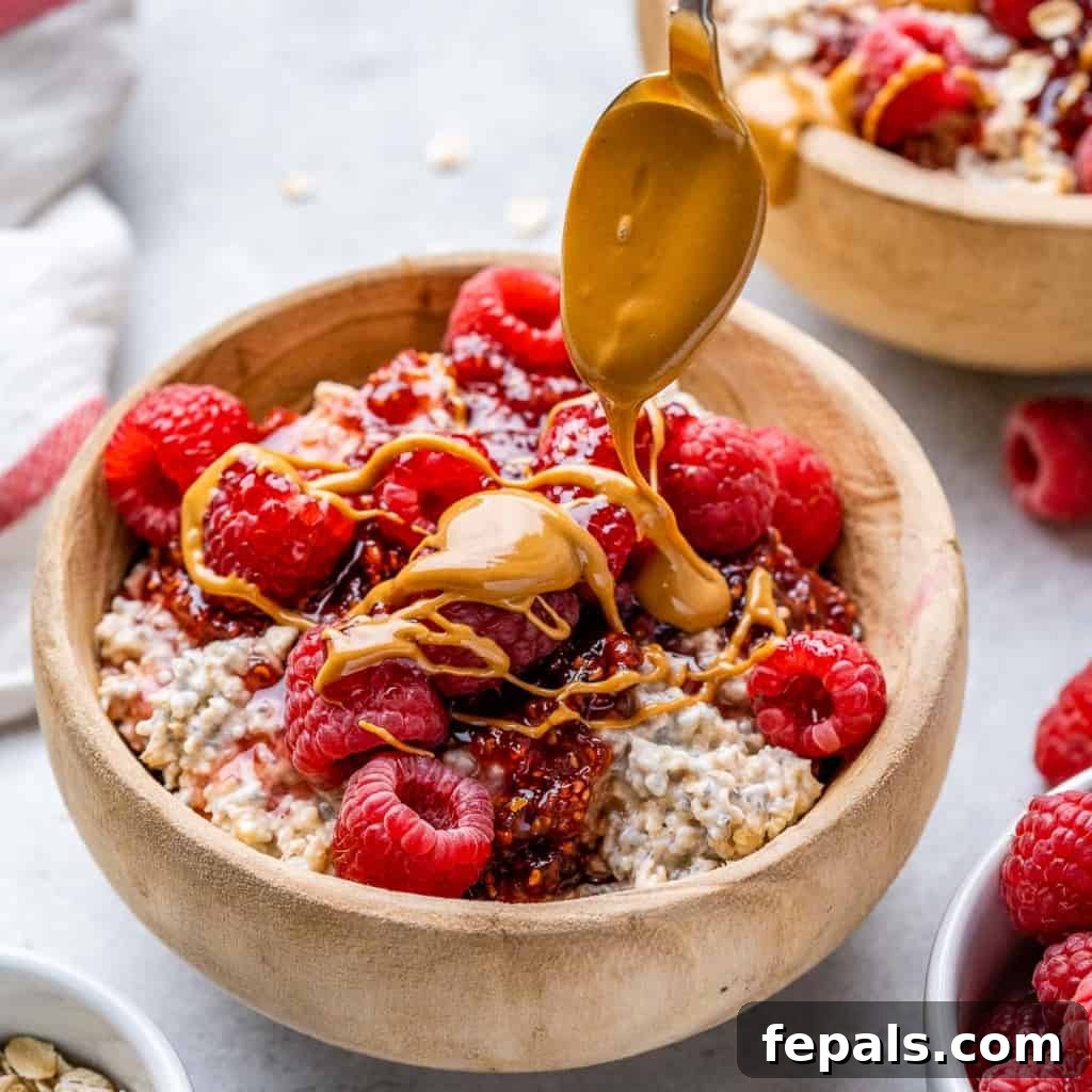 Dreamy PB&J Overnight Oats 9 side shot of creamy overnight oats in a brown wooden bowl topped with a rich peanut butter drizzle and fresh raspberries