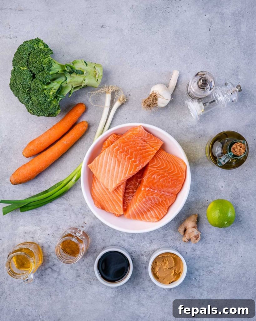 Umami Miso Salmon 4 Various fresh ingredients laid out for preparing miso glazed salmon, including salmon fillets, miso paste, ginger, garlic, soy sauce, honey, lime, sesame oil, broccoli, and carrots.