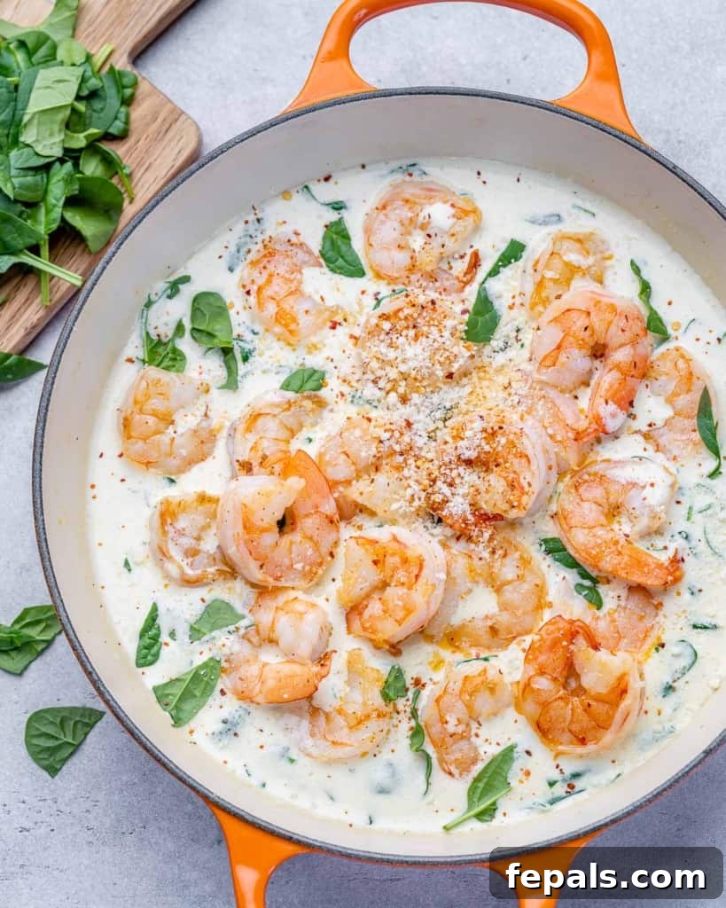 Top view of creamy sauteed shrimp with spinach in an orange skillet, ready to serve.