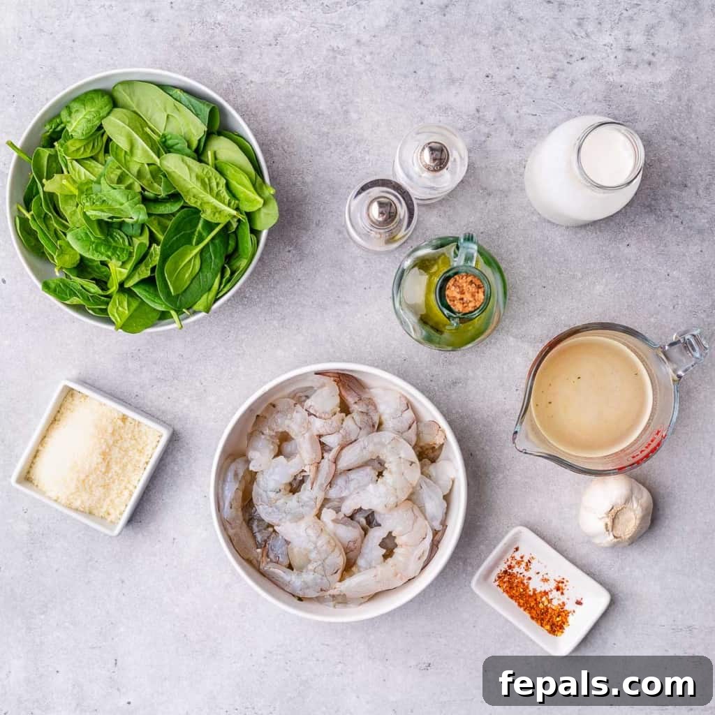 Collection of fresh ingredients for creamy keto shrimp skillet: shrimp, spinach, garlic, parmesan, cream, and oil.