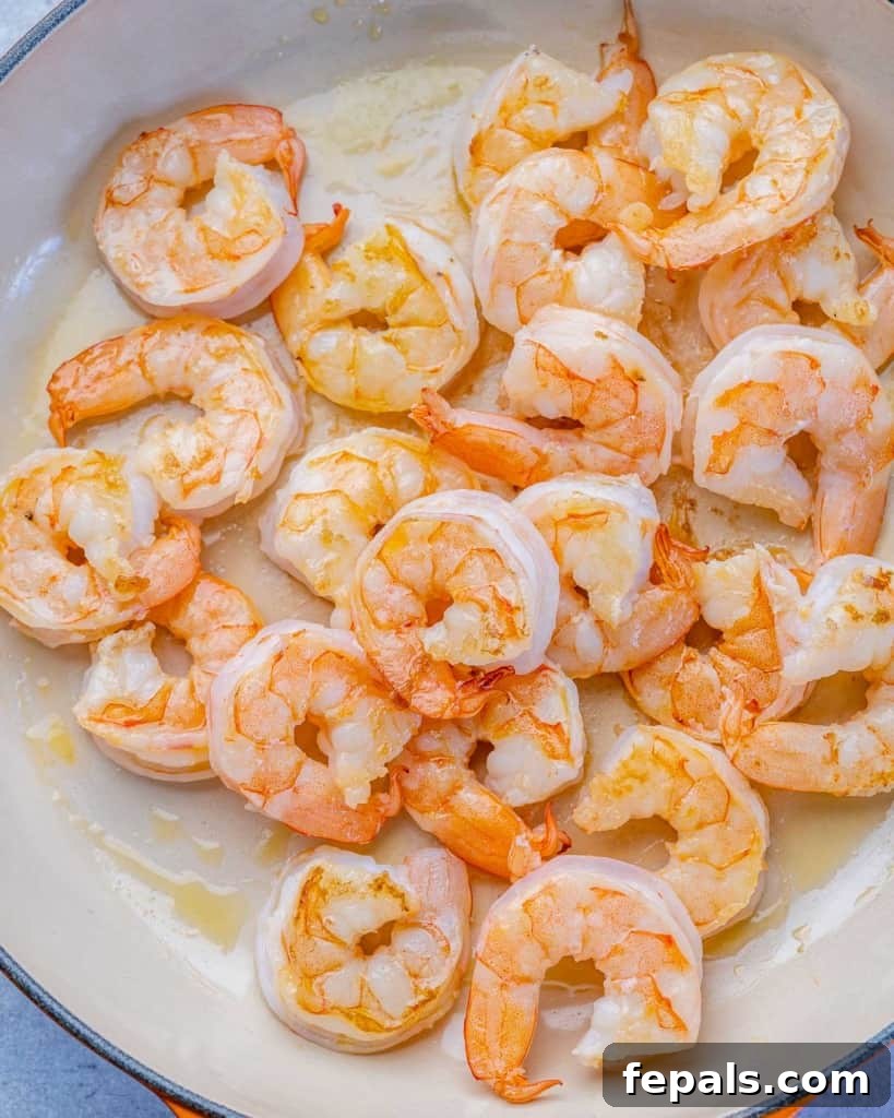 Shrimp being sautéed in a hot pan with oil, turning pink.