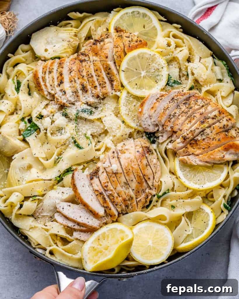 Top view of a skillet filled with creamy lemon garlic pasta topped with sliced chicken breast and fresh parsley.